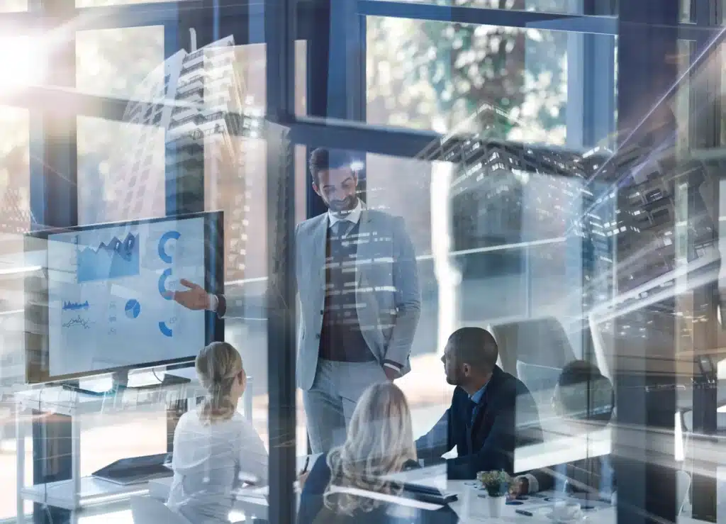 Business professionals gathered in a meeting room, discussing ideas in front of a large presentation screen.