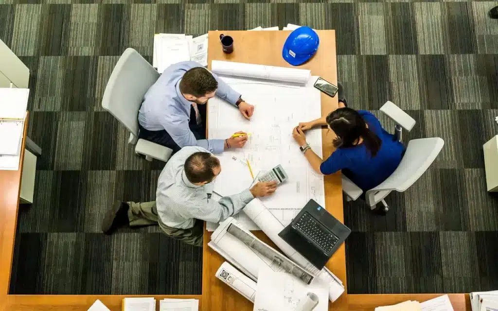 Strategic Interview Questions: A group of three people examines blueprints and documents at a table, engaged in discussion.
