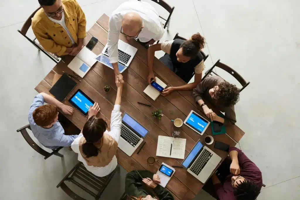 A group of diverse individuals seated around a table, each using a laptop, engaged in discussion and collaboration