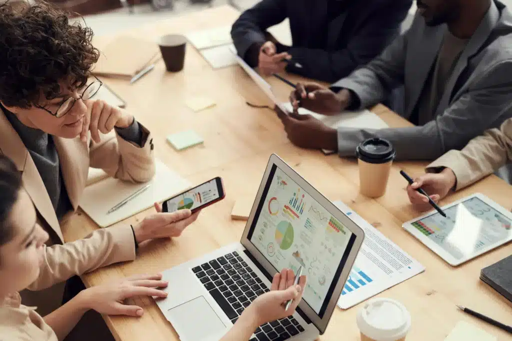 A team of individuals sitting together at a table, each with a laptop, collaborating on a project in a professional setting.