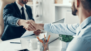 Two men engaged in a handshake at a desk, representing a formal agreement or collaboration.