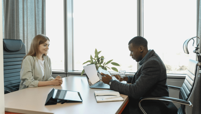 How to Hire Employees: A man and woman at an office table, collaborating on a project with papers and a laptop between them.